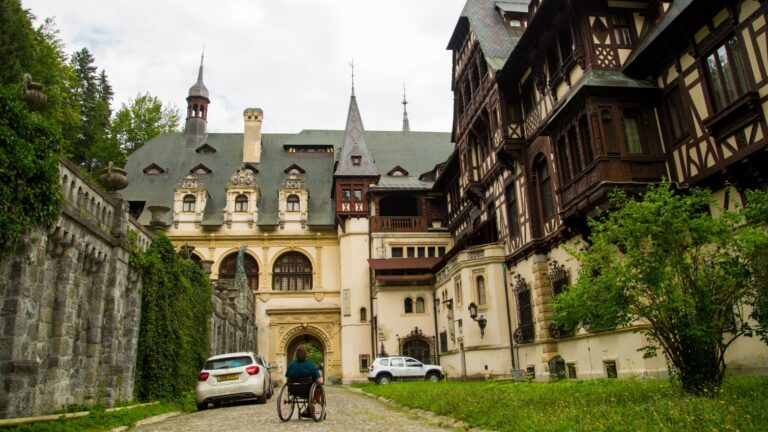 A wheelchair user stares up at the famous Peles Castle in Romania. They are round the back of the building.